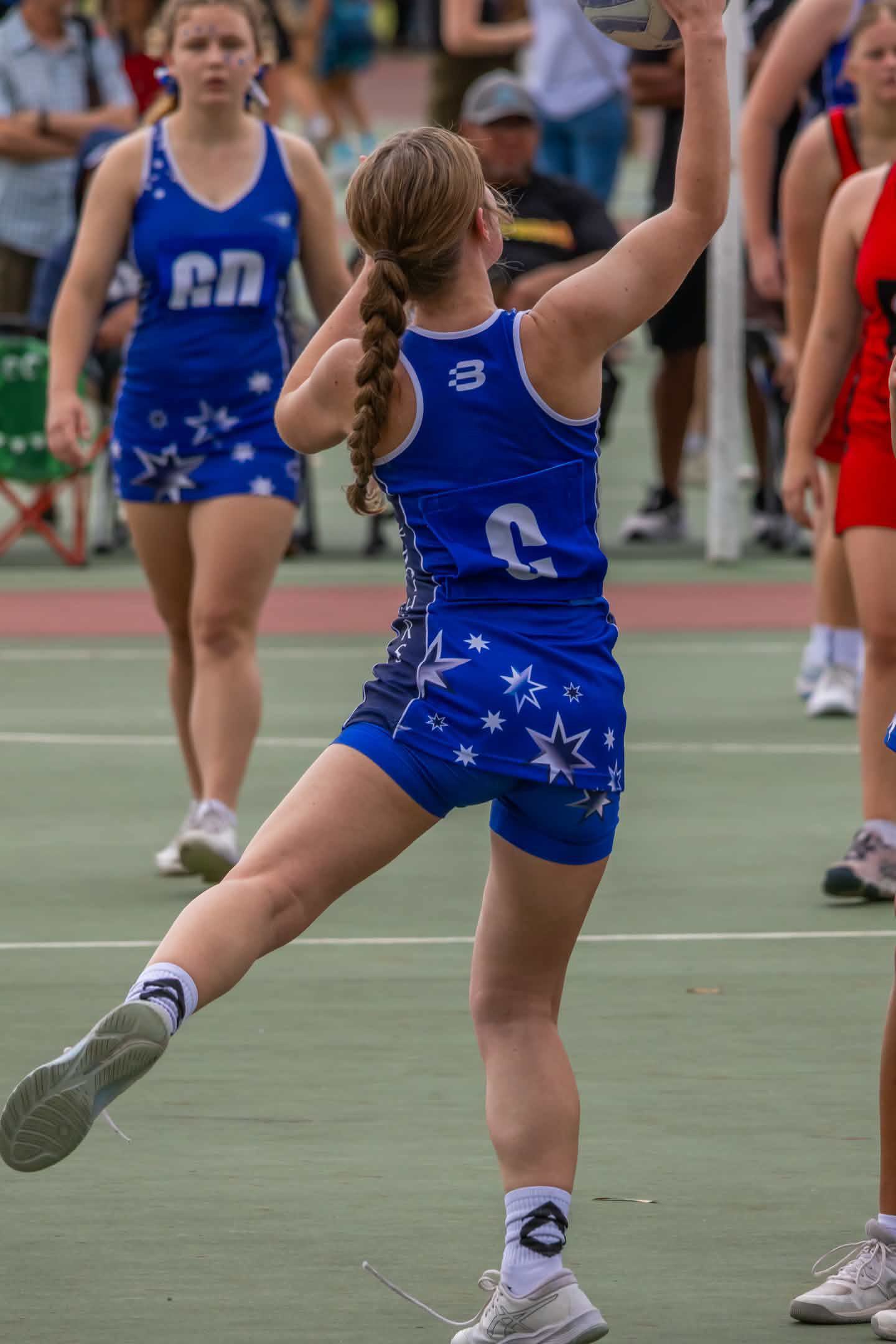Netball player in a blue uniform raising an arm on an outdoor court