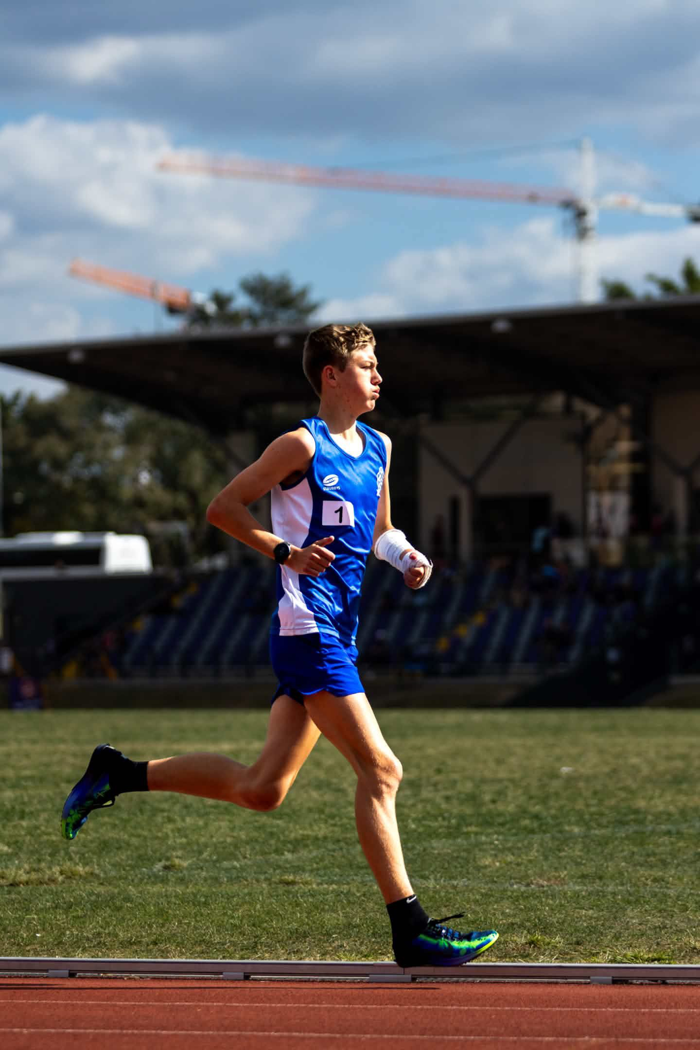 Athlete in blue running on a track under a bright sky
